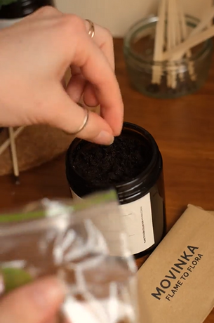 hand planting seeds into a an amber jar. Matches and a MOVINKA labelled seed packet in the background.